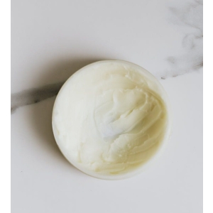 Creamy skincare product in round container on marble surface.