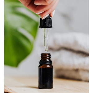 Luxury skincare serum dropper over brown glass bottle on wooden board.