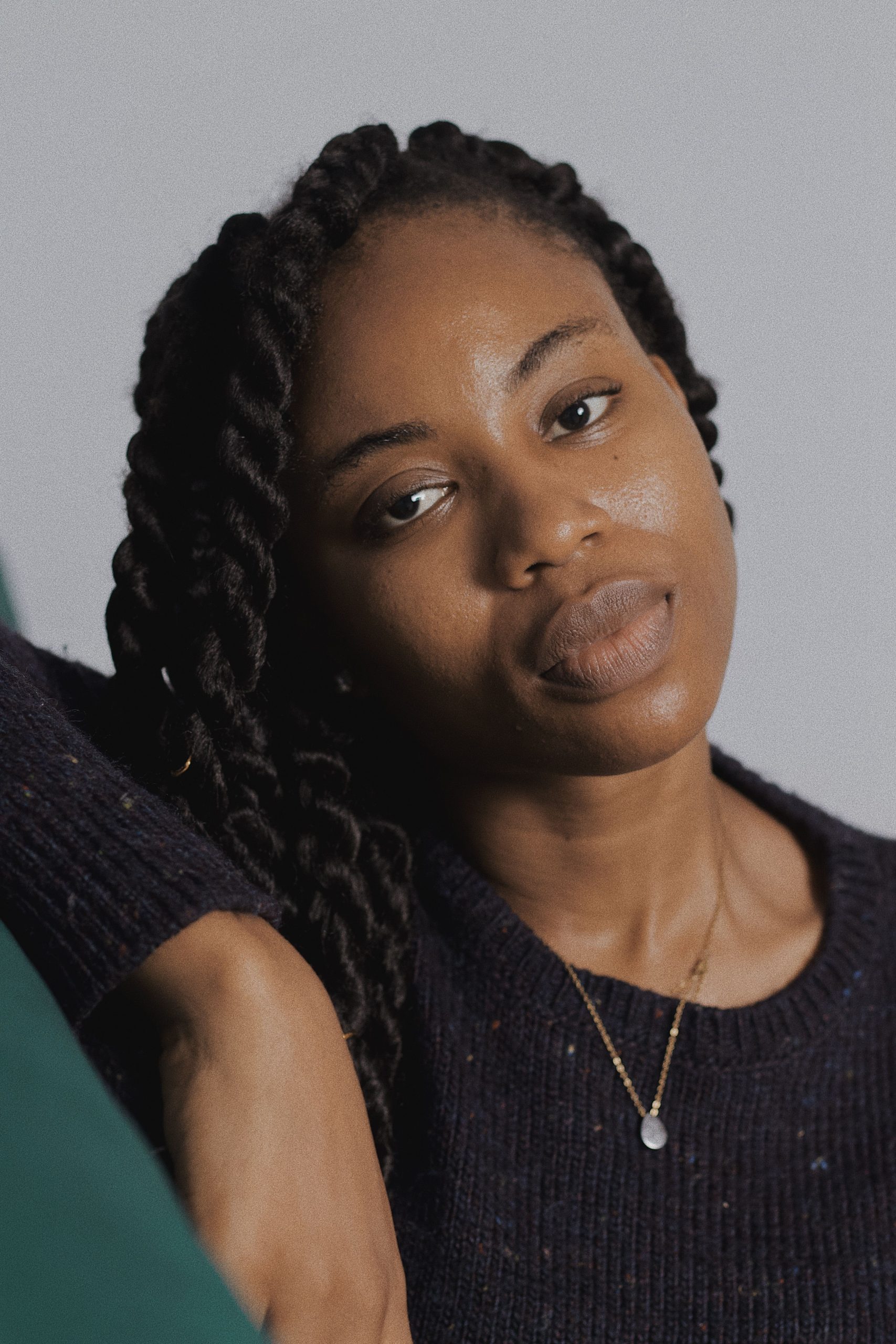 Close-up portrait of a woman with braided hair wearing a gold necklace and a relaxed expression.
